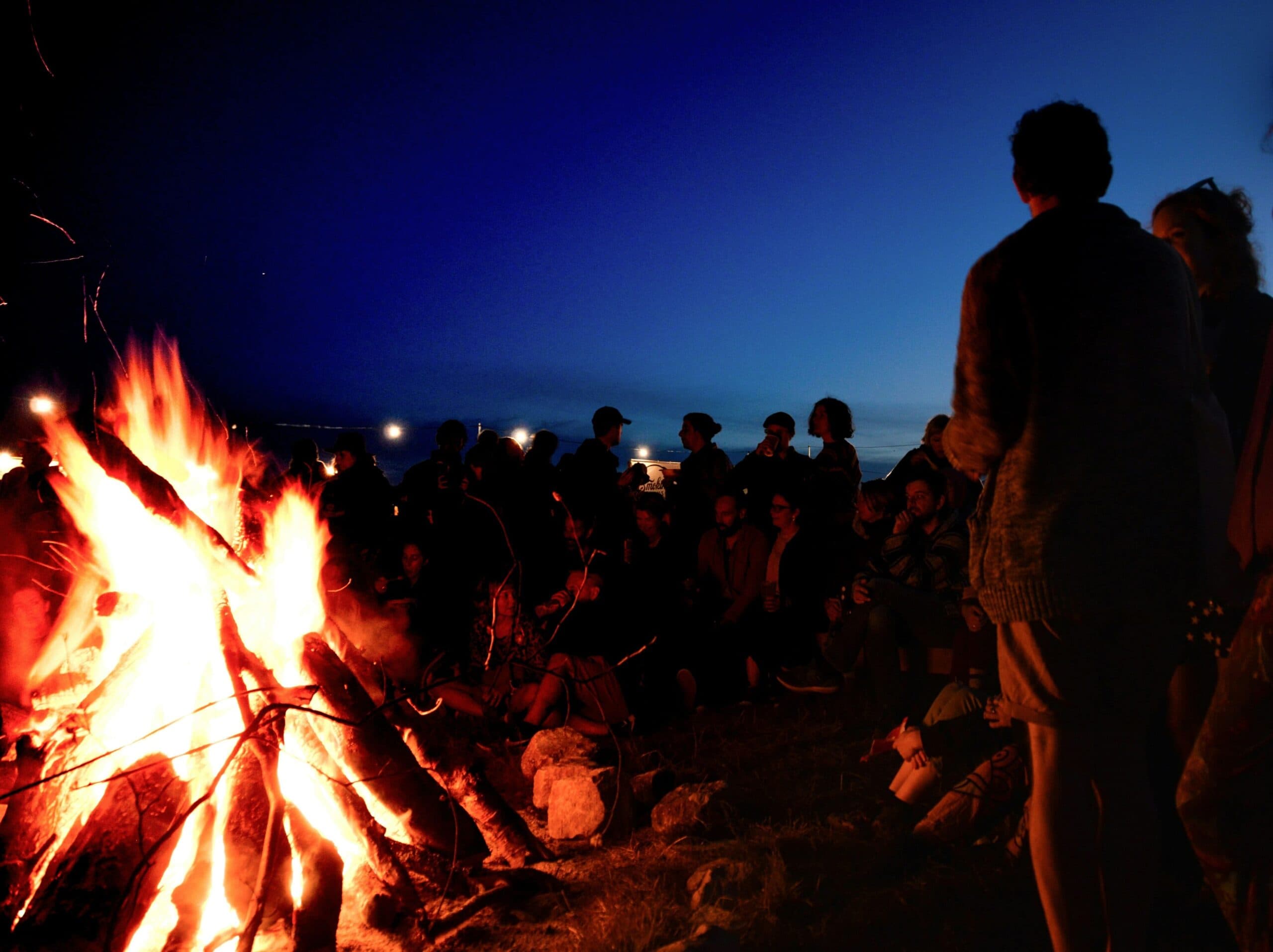 Large group of friends sit around a bonfire