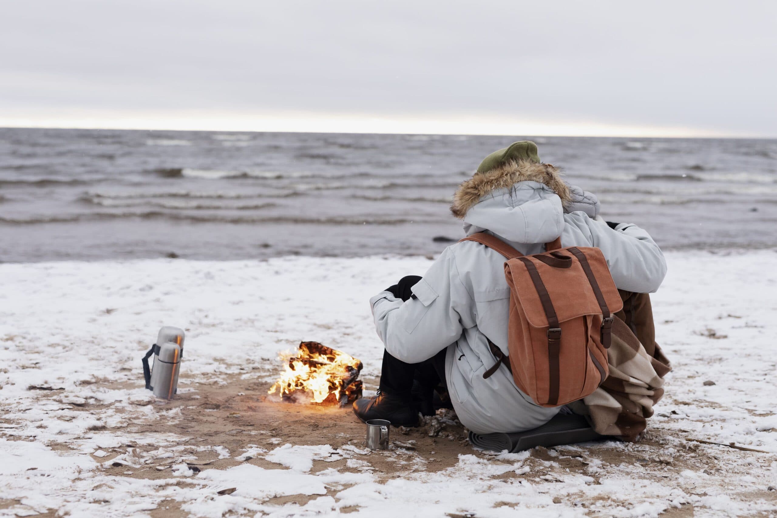 Traveler warms by fire on cold winter beach